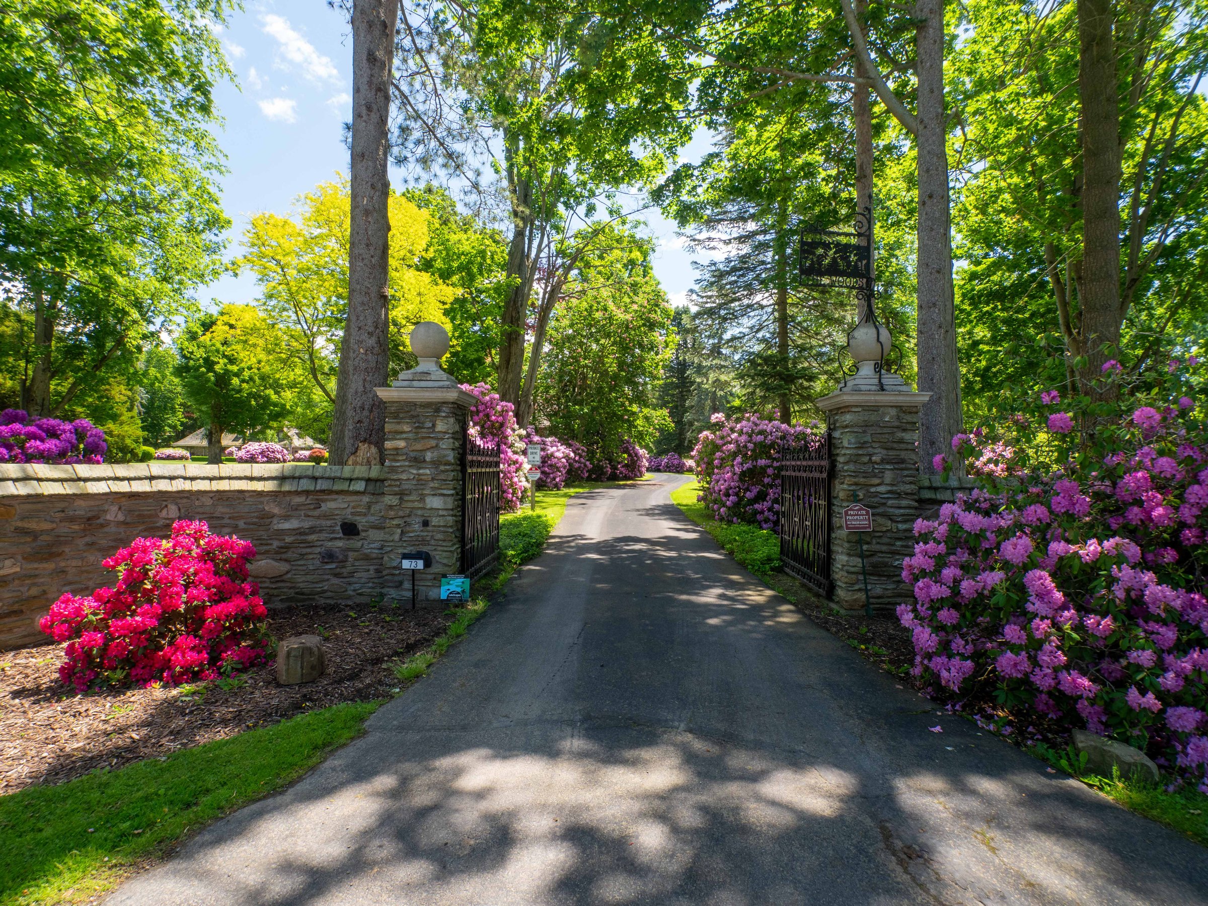 The stone-pillared front gates of The Woods at Bemus Point in spring bloom